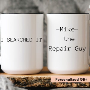 Puede incluir: Dos tazas de cerámica blanca con asas y bordes negros. La taza de la izquierda presenta el texto negro I SEARCHED IT. La taza de la derecha presenta el texto negro -Mike- the Repair Guy. Ambas tazas tienen forma cilíndrica y acabado liso.