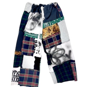 Può includere: Pantaloni patchwork con vita con coulisse. I pantaloni presentano una varietà di tessuti, tra cui scozzese, stampa leopardata e jersey grigio. Toppe di tessuto bianco presentano disegni e testo neri in stile graffiti. I pantaloni sono un mix di colori, tra cui blu navy, verde, rosso e grigio.