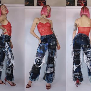 May include: Dark wash denim jeans with patchwork and distressed details. The jeans feature multiple fabric patches, white fringe, and black leather accents. The model is wearing a red lace top and red heels.