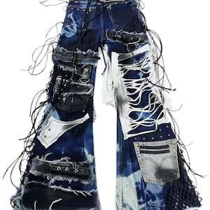 May include: Distressed blue denim jeans with multiple patches, rips, and black leather accents. The jeans feature a unique design with lace-up details, metal studs, and a pocket with a zipper. The overall style is edgy and unconventional.