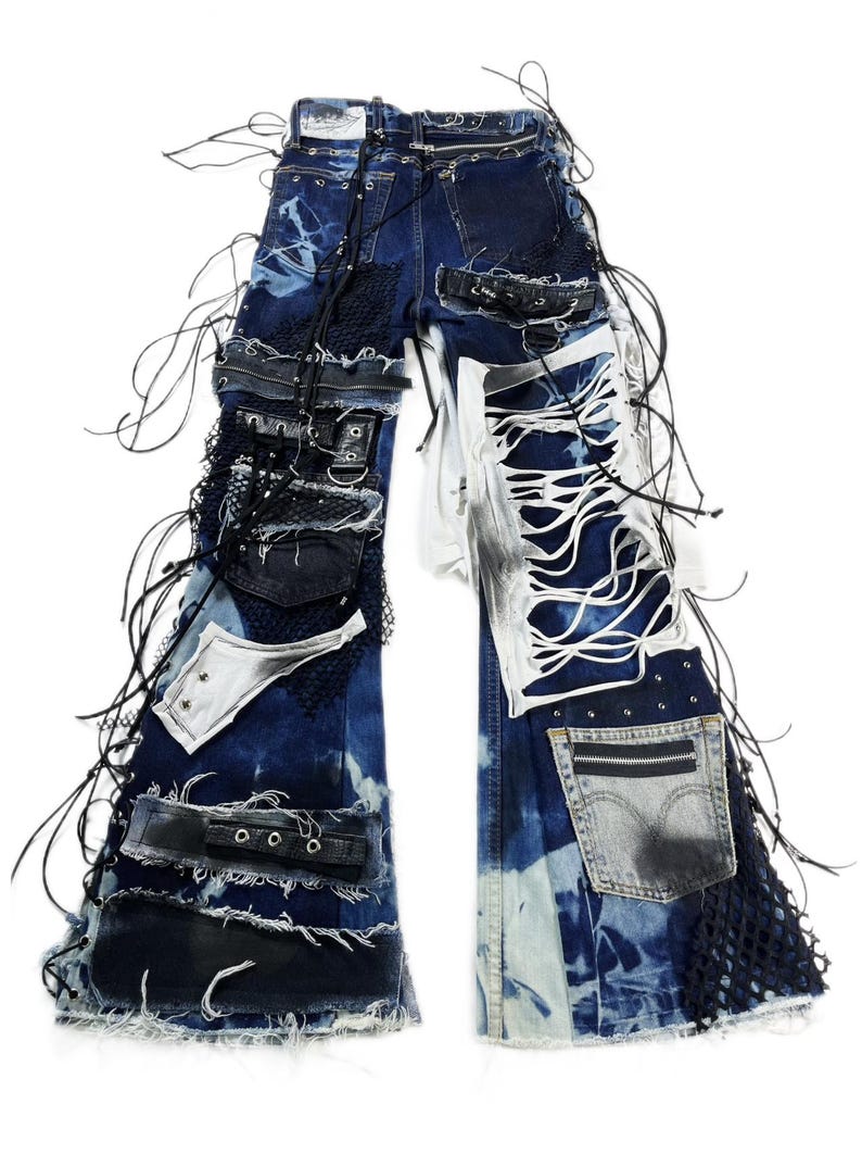 May include: Distressed blue denim jeans with multiple patches, rips, and black leather accents. The jeans feature a unique design with lace-up details, metal studs, and a pocket with a zipper. The overall style is edgy and unconventional.