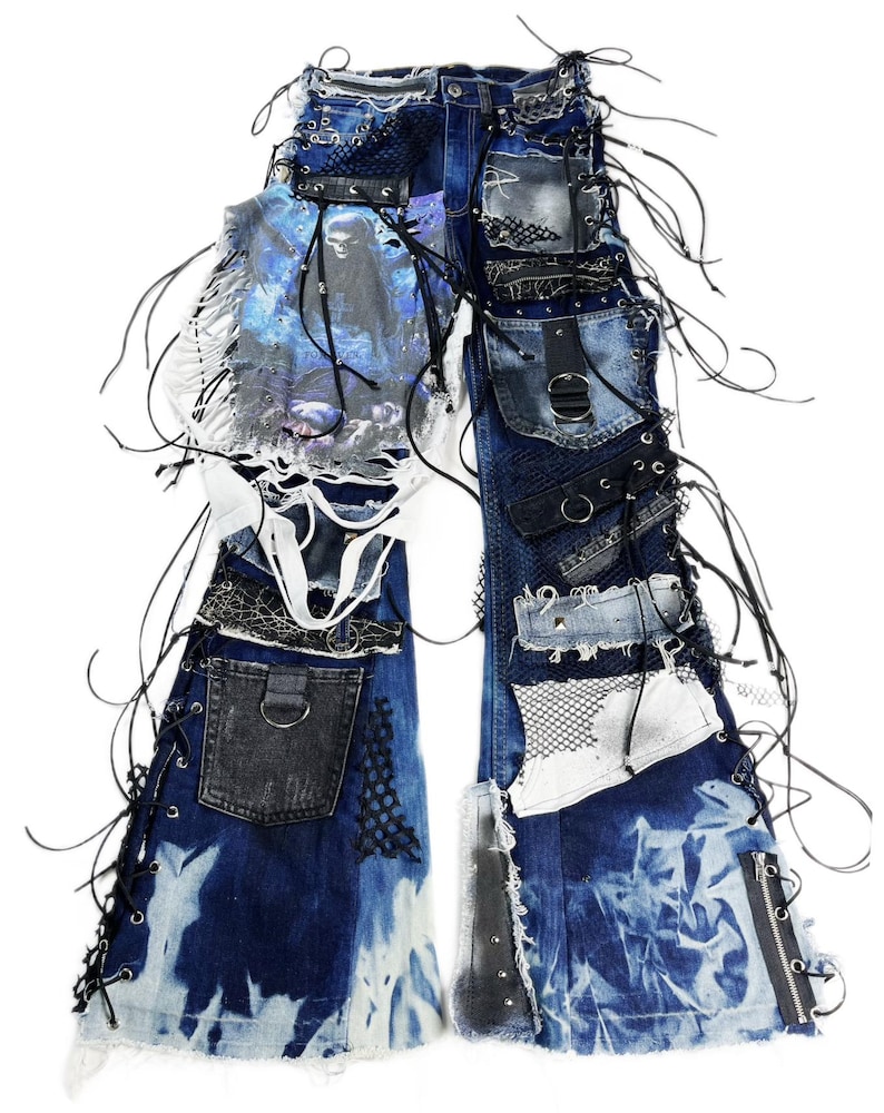 May include: Distressed denim jeans with multiple patches, lace-up details, and a skull graphic. The jeans feature a mix of textures, including mesh and leather accents, and are embellished with black cords and zippers.