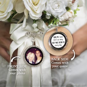May include: A silver wedding bouquet charm with a photo on the front and a quote on the back. The front side features a photo of two women, framed by a circle of clear crystals. The back side has the quote: "THOSE WE LOVE DON'T GO AWAY THEY WALK BESIDE US every day."
