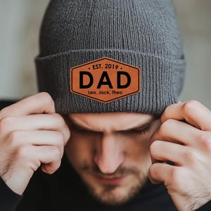 May include: Gray knitted beanie with a brown leather patch that says "EST. 2019. DAD Leo, Jack, Theo"