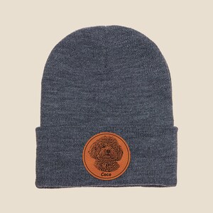 May include: A dark gray beanie with a brown leather patch featuring a dog's portrait and the name "Coco".