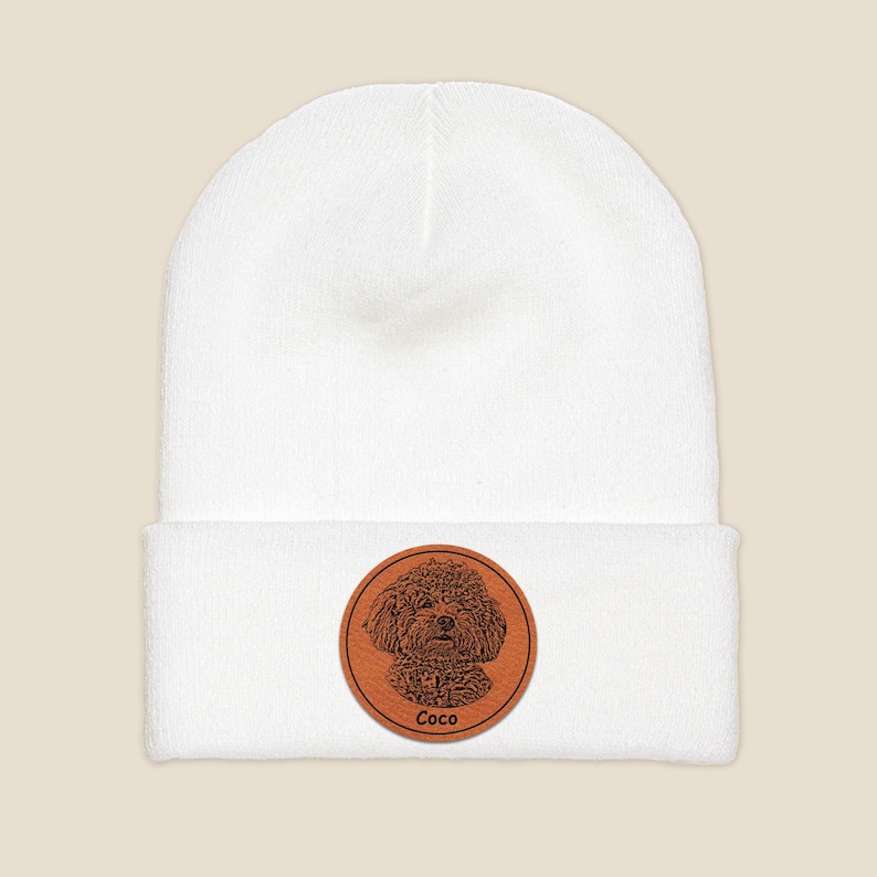 May include: White knit beanie with a brown leather patch featuring a black and white illustration of a dog with the name "Coco" written below.