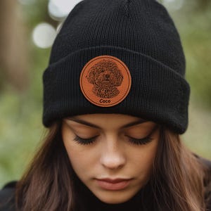 May include: Black beanie with a brown leather patch featuring a dog's face and the name "Coco" in white text.
