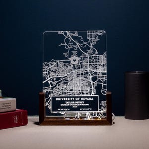 May include: A white acrylic light-up sign with a map of the University of Nevada campus. The sign has a graduation cap icon and text that reads "University of Nevada", "Taylor Petrey", "Bachelor of Science in Nursing", "2025", "33°59'37.6"N", and "81°01'47.7"W".