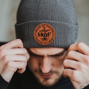 May include: A gray beanie with a brown leather patch that says "Man of Faith" with a cross and the letters "MOF" and "Rooted in Christ".
