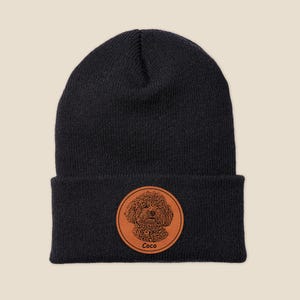 May include: Black knit beanie with a brown leather patch featuring a dog portrait and the name "Coco" in white text.