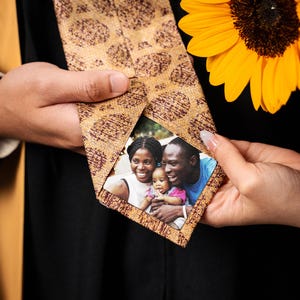 May include: A gold tie with a brown and gold pattern. The tie has a small photo of a family of three, a woman, a man, and a child, with a green background.