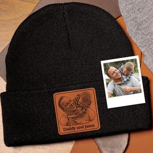 May include: Black knit beanie with a brown leather patch featuring a photo of a father and son. The patch has the text "Daddy and Jason" below the photo.