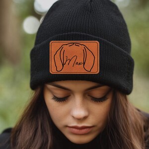 May include: Black beanie with a brown leather patch featuring a dog silhouette and the name "Max" in cursive.