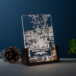 May include: A clear acrylic map of the University of Nevada, with a heart symbol. The map is illuminated and set in a dark wooden base. Text includes the university name, a name, degree, and coordinates.