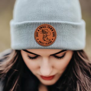 May include: A light blue beanie with a brown leather patch that says "Just a small town girl" with a boot and sunflower design. The patch also includes the names "Emily Claire".