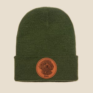 May include: A green knitted beanie with a brown leather patch featuring a dog's face and the name "Coco".