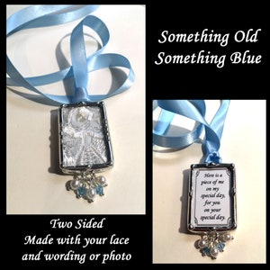 May include: A two-sided rectangular pendant with a silver frame, white lace, and a light blue ribbon. The pendant has a cluster of pearls and blue beads. Text on the pendant reads "Here is a piece of me on my special day, for you on your special day."