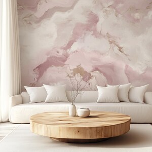May include: A white sofa with white cushions sits in front of a pink and white abstract marble wallpaper. A round wooden coffee table sits in front of the sofa with a small white vase and a small white bowl on top.