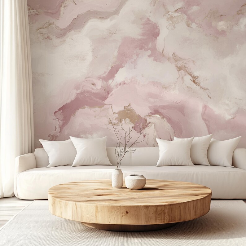 May include: A white sofa with white cushions sits in front of a pink and white abstract marble wallpaper. A round wooden coffee table sits in front of the sofa with a small white vase and a small white bowl on top.
