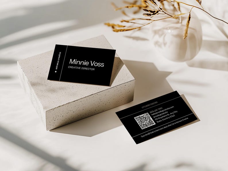 May include: Black business cards with white text, including the name "Minnie Voss, Creative Director." One card rests on a concrete block, another lies flat. The cards feature a QR code and contact information. The background is white with shadows.