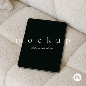 May include: A black tablet computer with a white "MOCKUP" text overlay and the words "PSD smart object" displayed on a white fluffy surface.