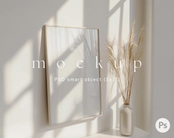 May include: A white frame mockup with a light background and a vase with dried pampas grass. The text "mockup" and "PSD smart object (5x7)" is visible in the image.