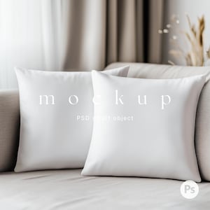 以下が含まれることがあります： 薄いベージュのソファに置かれた白いクッション2つ。1つのクッションには「mockup」と「PSD smart object」の文字が書かれている。
