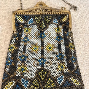 May include: Vintage beaded handbag with a decorative metal frame and chain strap. The bag features a geometric pattern in black, white, yellow, and blue beads. The frame has an ornate, filigree design.