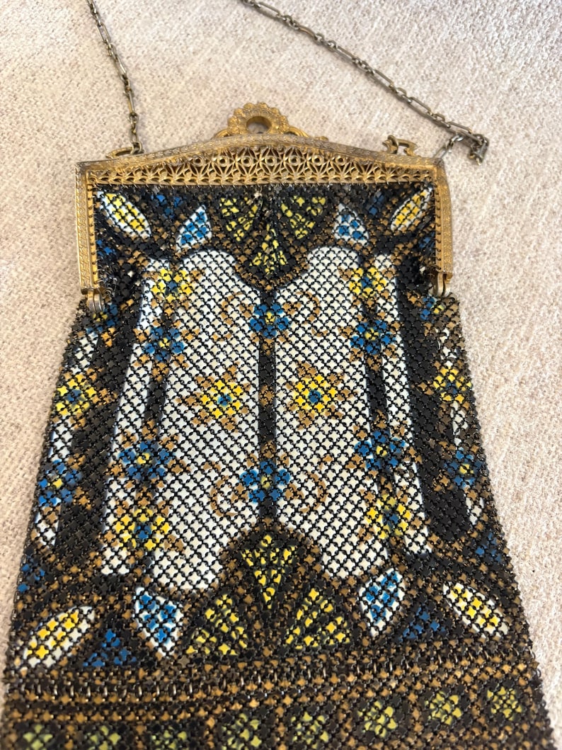 May include: Vintage beaded handbag with a decorative metal frame and chain strap. The bag features a geometric pattern in black, white, yellow, and blue beads. The frame has an ornate, filigree design.