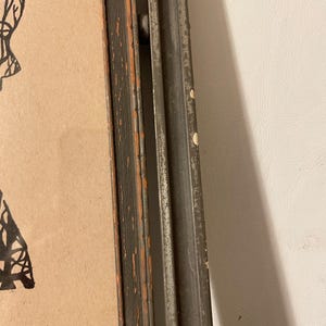 May include: A black and white framed drawing of a person with a detailed design. The frame is distressed and has a dark gray finish.