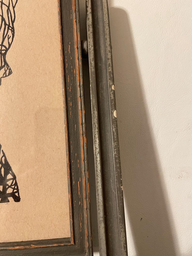 May include: A black and white framed drawing of a person with a detailed design. The frame is distressed and has a dark gray finish.