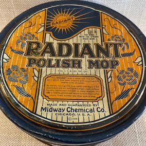 May include: Vintage Radiant Polish Mop tin with a navy blue rim and an orange and black design. The text on the tin reads "Radiant Polish Mop" and "Midway Chemical Co. Chicago, U.S.A. 1926".
