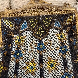 May include: An antique metal mesh handbag with a gold-toned frame and chain. The mesh is black, white, yellow, and blue, with a floral pattern. The frame has an ornate, filigree design.
