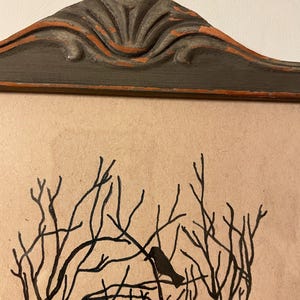 May include: A black and white illustration of a tree with birds perched on the branches. The illustration is framed in a dark gray frame with a decorative top.