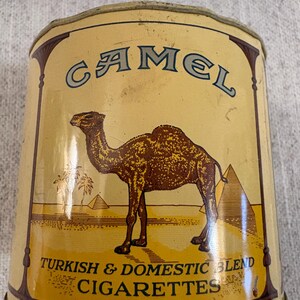 May include: Vintage Camel cigarette tin with a tan and brown color scheme. The tin features a camel illustration, pyramids, and the text "Camel Turkish & Domestic Blend Cigarettes."