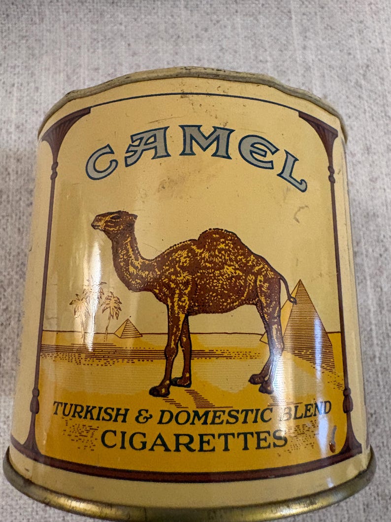 May include: Vintage Camel cigarette tin with a tan and brown color scheme. The tin features a camel illustration, pyramids, and the text "Camel Turkish & Domestic Blend Cigarettes."