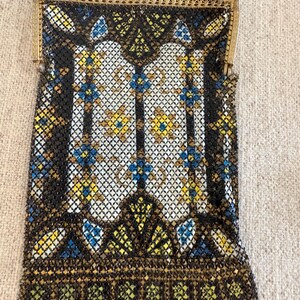 May include: An antique beaded handbag with a gold-tone frame and chain. The bag features a black mesh background with a geometric pattern in white, yellow, and blue. The bottom edge has a scalloped design.