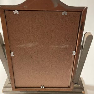 May include: A wooden picture frame with a brown backing and a gray frame. The frame has a decorative top and a stand on the back.
