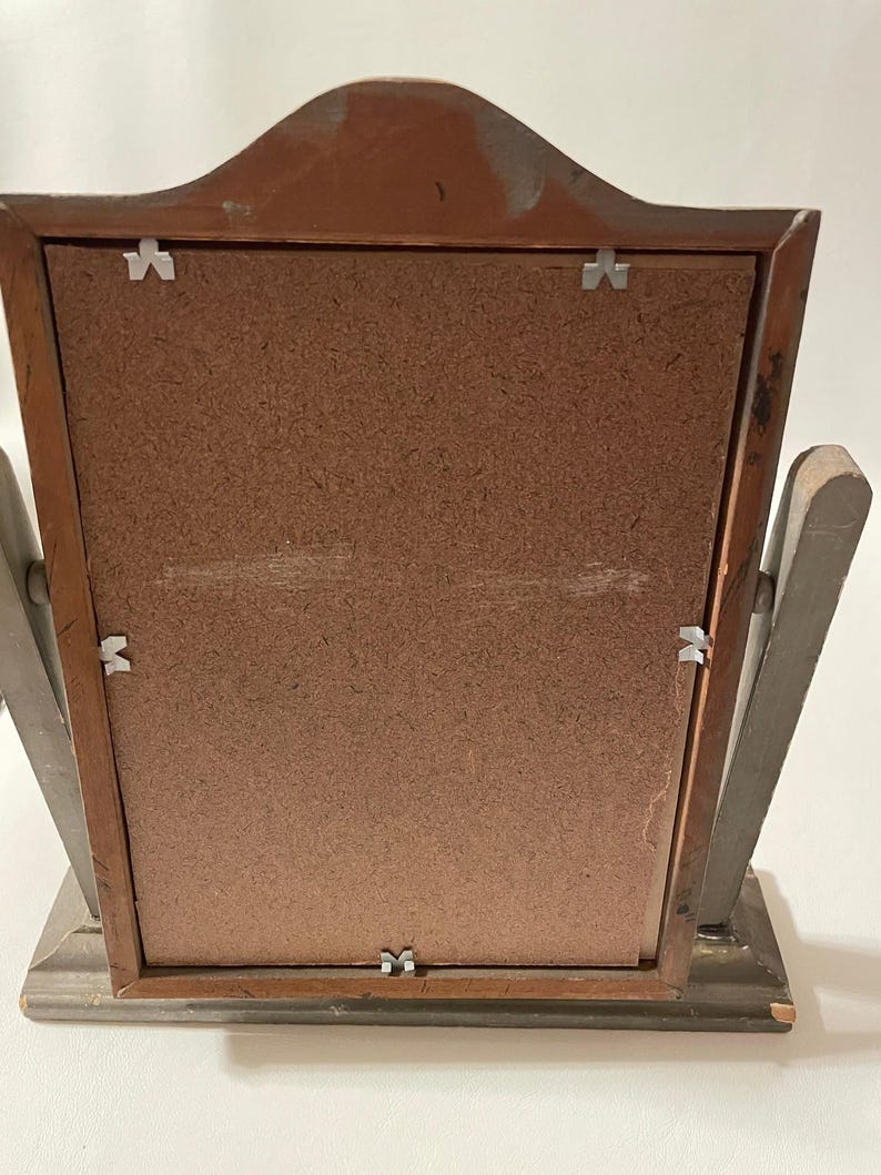 May include: A wooden picture frame with a brown backing and a gray frame. The frame has a decorative top and a stand on the back.