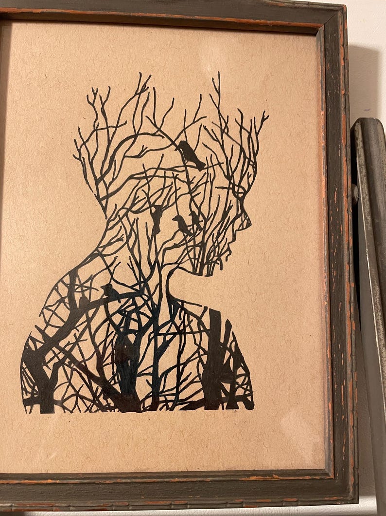 May include: A black and white silhouette of a person's head and shoulders, with a tree-like pattern inside. The silhouette is framed in a dark wood frame.