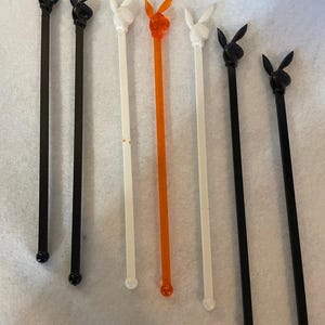 May include: Eight cocktail stirrers with a bunny head design.  Two are black, two are white, one is orange, and three are black.