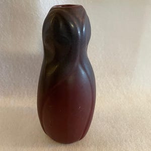 May include: A dark red and black ceramic vase with a unique, organic shape. The vase has a smooth, glossy finish and is perfect for displaying flowers or other decorative items.