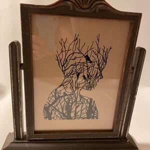 May include: A framed silhouette print of a person with branches and birds inside their head. The frame is dark brown wood with a distressed finish.
