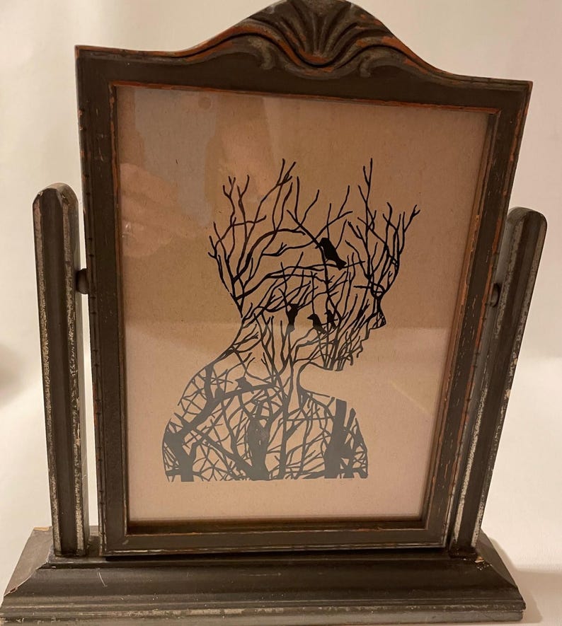 May include: A framed silhouette print of a person with branches and birds inside their head. The frame is dark brown wood with a distressed finish.