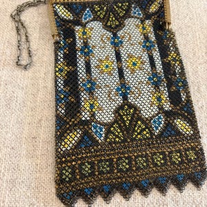 May include: Vintage black mesh handbag with a decorative gold-tone frame and chain strap. The bag features a detailed pattern with white, yellow, and blue accents. The bottom edge has a scalloped design.