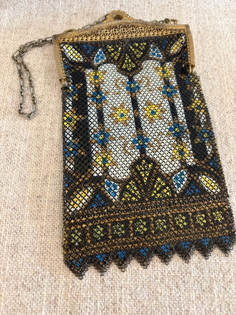 May include: Vintage black mesh handbag with a decorative gold-tone frame and chain strap. The bag features a detailed pattern with white, yellow, and blue accents. The bottom edge has a scalloped design.