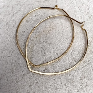 Op de afbeelding: Een paar gouden oorringen met een gehamerde textuur. De oorringen zijn groot en hebben een licht ovale vorm.