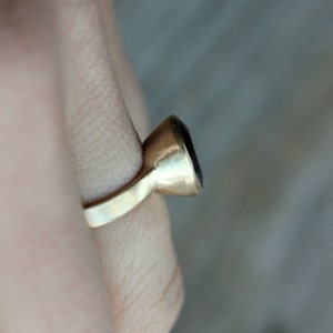Puede incluir: Un anillo de oro con una piedra preciosa de color p&uacute;rpura oscuro. El anillo est&aacute; en un dedo.