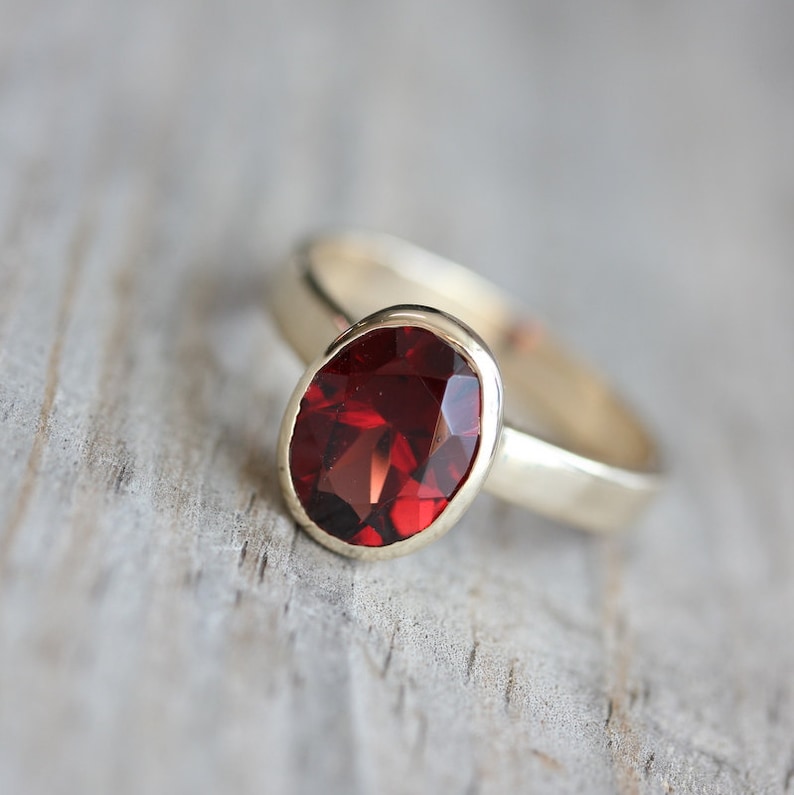 Puede incluir: Un anillo de oro con una gran piedra preciosa roja de forma ovalada engastada en un engaste de bisel.
