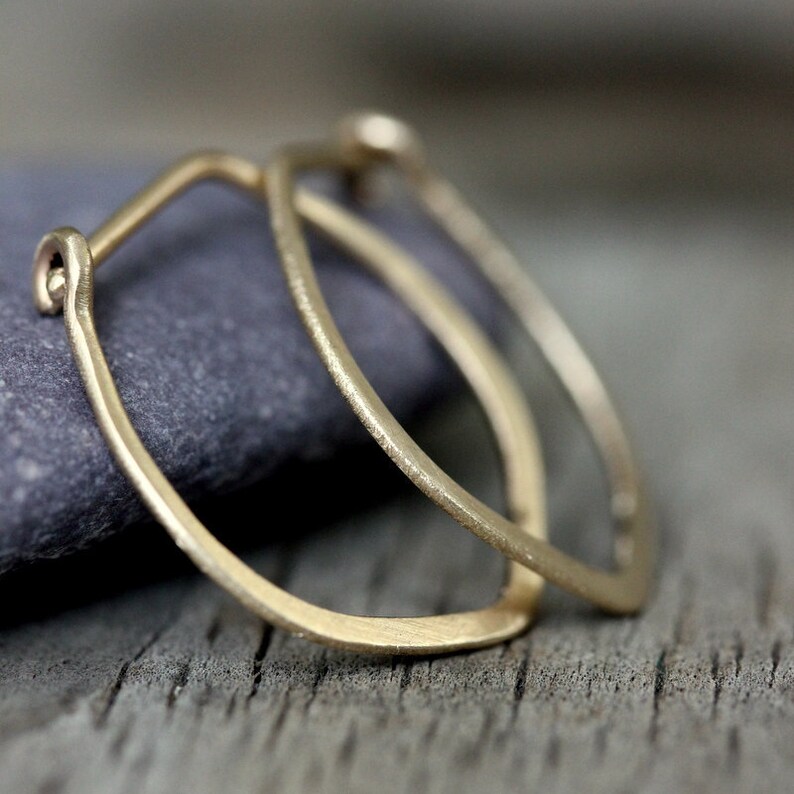 Op de afbeelding: Een paar gouden oorringen met een licht ovale vorm. De oorringen zijn gemaakt van dik, getextureerd draad.